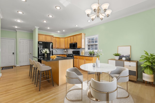 kitchen with decorative backsplash, light wood-style floors, dark countertops, black appliances, and a sink