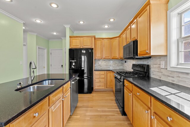 kitchen with tasteful backsplash, light wood-style floors, a sink, dark stone countertops, and black appliances