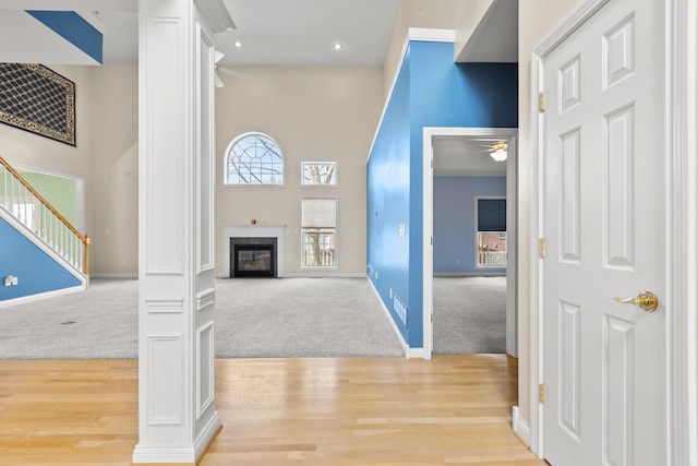 living room featuring light carpet, a ceiling fan, baseboards, light wood-type flooring, and a glass covered fireplace