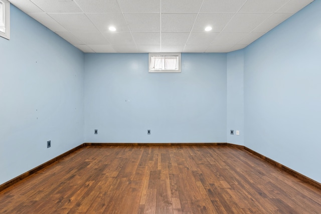 below grade area featuring dark wood-type flooring, recessed lighting, a drop ceiling, and baseboards