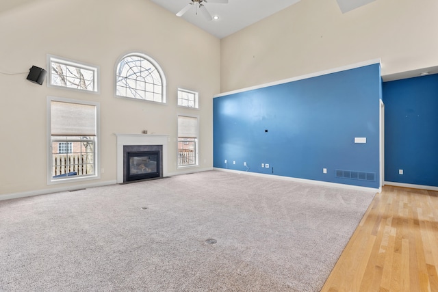 unfurnished living room with high vaulted ceiling, a fireplace with flush hearth, visible vents, baseboards, and a ceiling fan