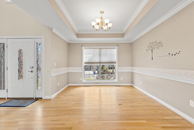 foyer entrance featuring crown molding, a raised ceiling, wood finished floors, a chandelier, and baseboards