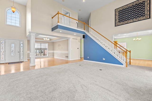 unfurnished living room with carpet flooring, a notable chandelier, stairway, and ornate columns