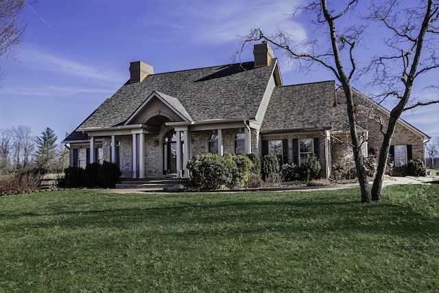 view of front of property featuring roof with shingles, a front lawn, a chimney, and brick siding