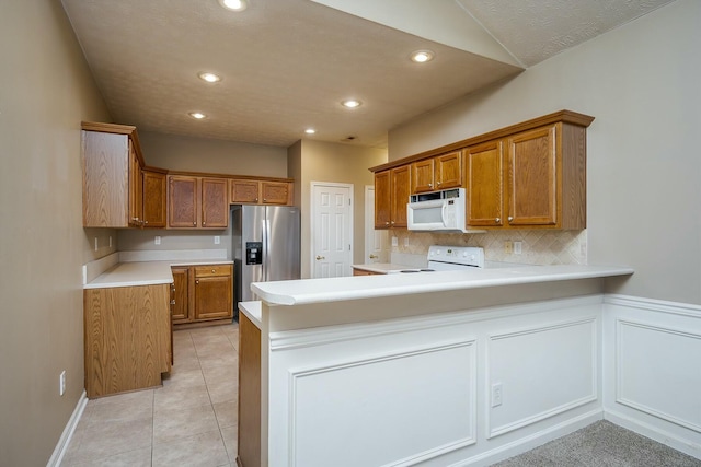 kitchen featuring brown cabinetry, stainless steel fridge, range with electric stovetop, and white microwave