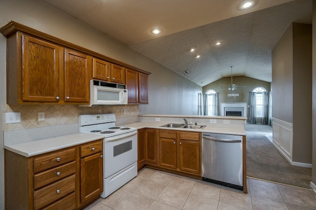 kitchen with a peninsula, white appliances, brown cabinetry, and a sink