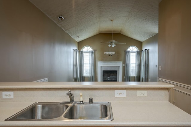 kitchen with lofted ceiling, ceiling fan, a sink, visible vents, and a glass covered fireplace