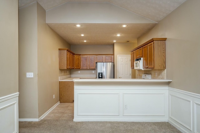 kitchen featuring light countertops, white microwave, light carpet, a peninsula, and stainless steel fridge with ice dispenser