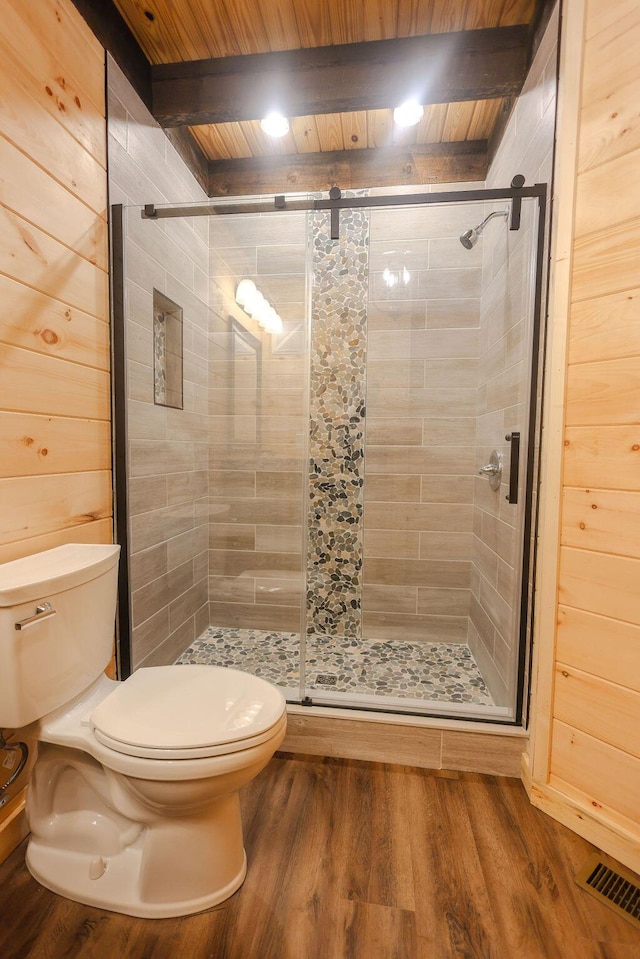 bathroom with a stall shower, toilet, wood finished floors, beamed ceiling, and wood walls