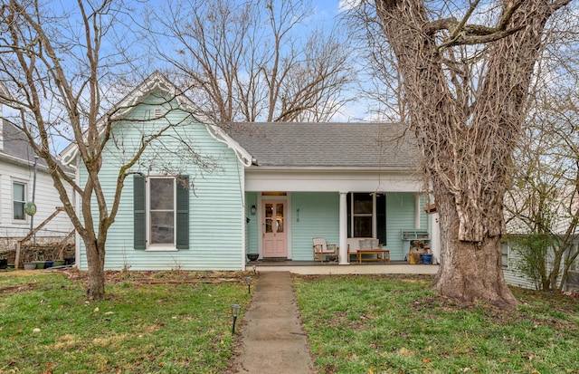 view of front facade with a porch, a shingled roof, and a front lawn