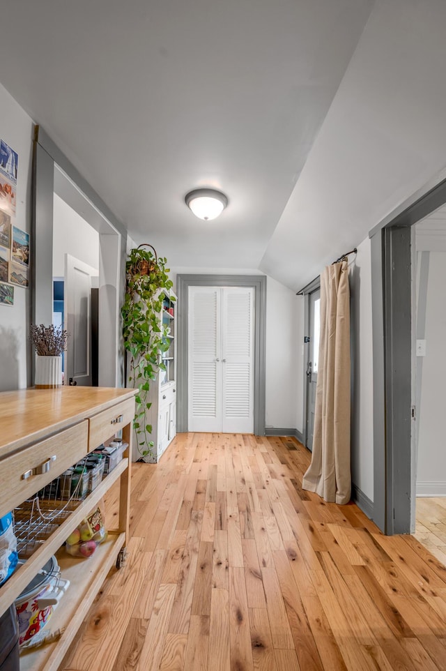 corridor featuring baseboards, lofted ceiling, and light wood-style floors