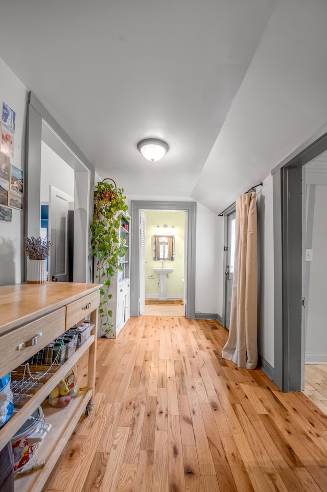 corridor with lofted ceiling, light wood-type flooring, and baseboards