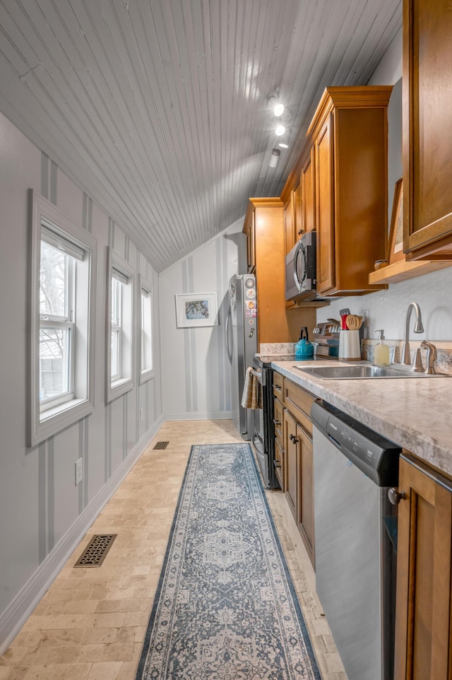 kitchen with lofted ceiling, brown cabinets, stainless steel appliances, light countertops, and a sink