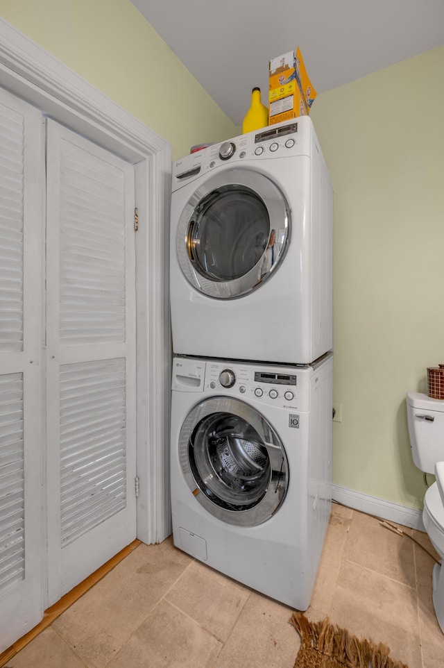 clothes washing area with laundry area, tile patterned flooring, stacked washer and clothes dryer, and baseboards