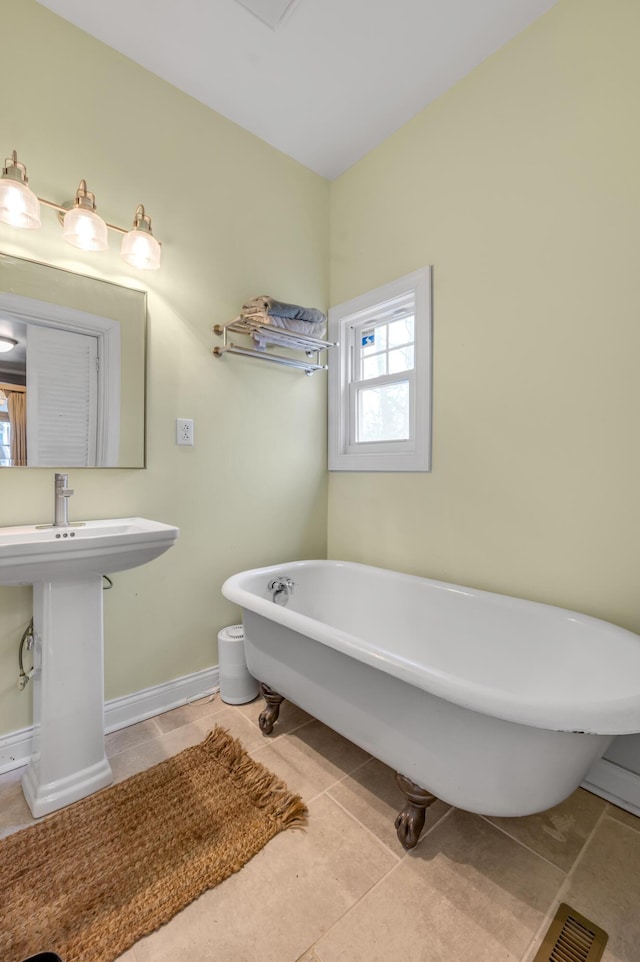 full bath with a soaking tub, tile patterned flooring, baseboards, and a sink