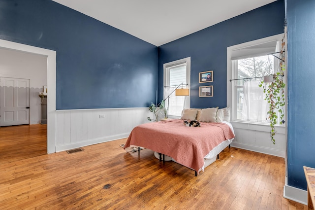 bedroom featuring a wainscoted wall, visible vents, baseboards, and hardwood / wood-style floors