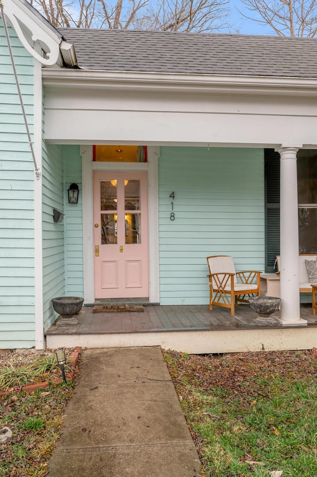 view of exterior entry with a porch and a shingled roof