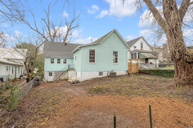 rear view of property featuring central AC unit, a shingled roof, and fence