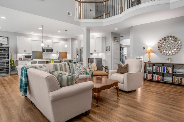 living room with light wood-style floors, recessed lighting, visible vents, and ornate columns