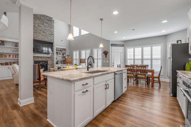 kitchen with wood finished floors, decorative light fixtures, stainless steel appliances, white cabinetry, and a sink