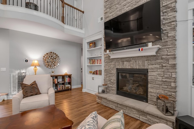 living area featuring a towering ceiling, a stone fireplace, wood finished floors, and visible vents