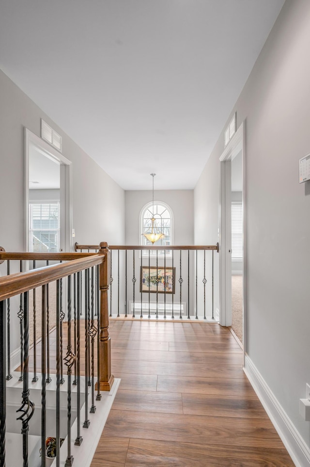 corridor featuring visible vents, baseboards, a wealth of natural light, and wood finished floors