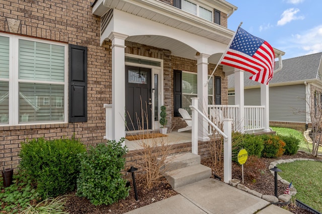 doorway to property with a porch and brick siding