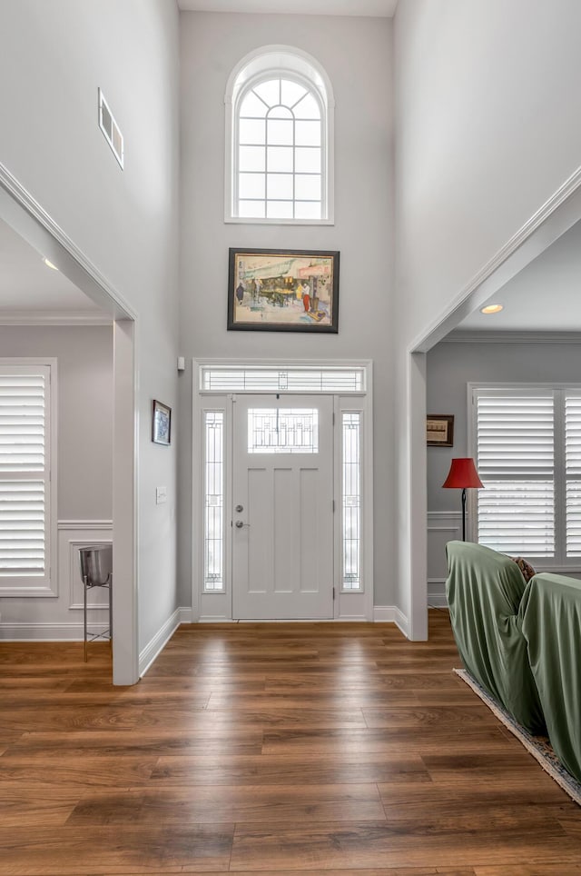 foyer featuring a wealth of natural light, visible vents, a towering ceiling, and wood finished floors