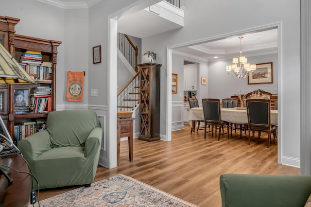 living area with stairs, light wood finished floors, an inviting chandelier, and crown molding