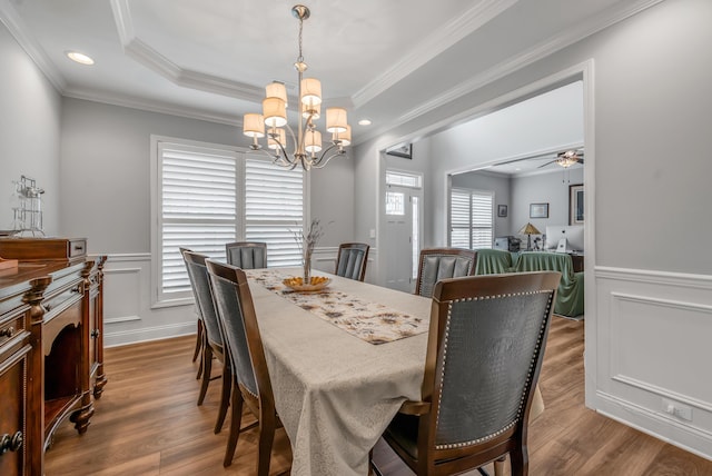 dining space with wood finished floors, a raised ceiling, and crown molding