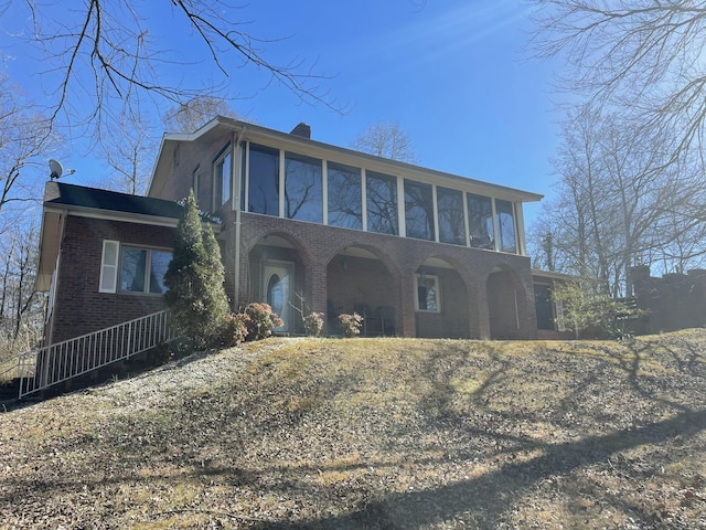 view of front facade with brick siding, a chimney, and a sunroom