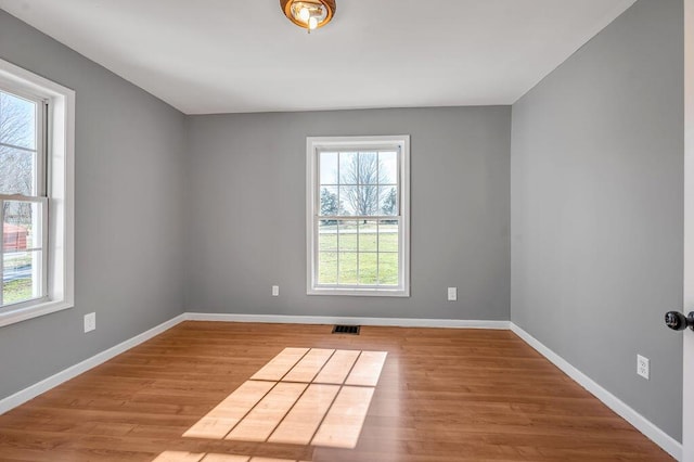 empty room featuring wood finished floors, visible vents, and baseboards