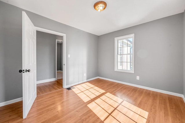 spare room featuring light wood-style floors, visible vents, and baseboards