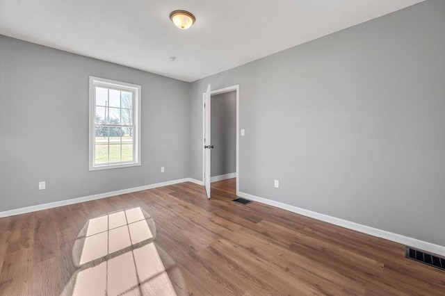 empty room with baseboards, visible vents, and wood finished floors