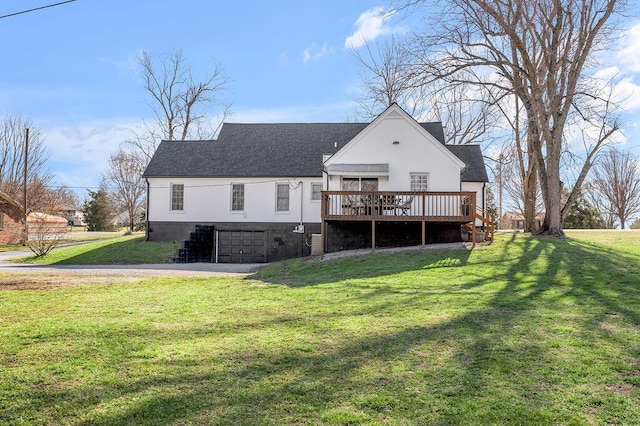 rear view of property featuring a garage, a wooden deck, roof with shingles, and a yard