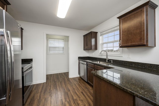 kitchen with a sink, dark wood-style floors, dark brown cabinets, appliances with stainless steel finishes, and dark stone counters