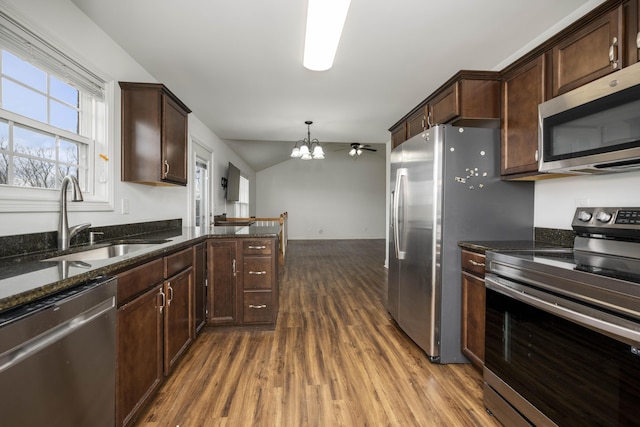 kitchen featuring dark wood-style floors, appliances with stainless steel finishes, a sink, dark brown cabinetry, and dark stone counters