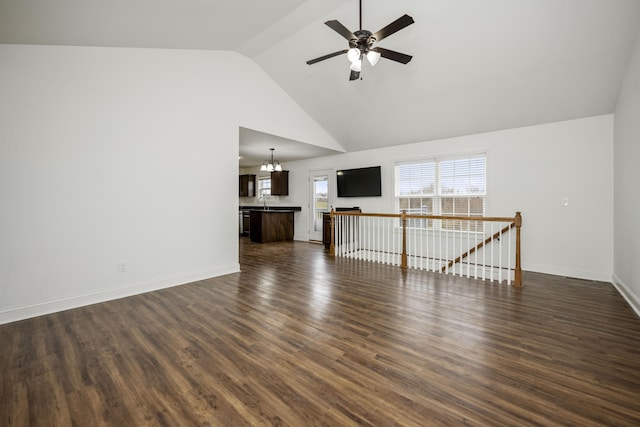 unfurnished living room featuring ceiling fan with notable chandelier, high vaulted ceiling, dark wood-type flooring, and baseboards