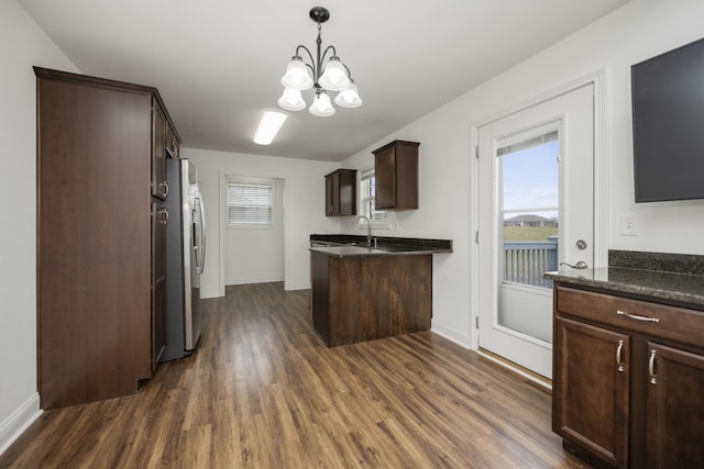 kitchen with dark wood-type flooring, freestanding refrigerator, an inviting chandelier, dark brown cabinets, and a sink