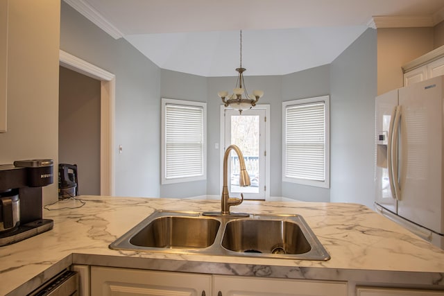 kitchen featuring white refrigerator with ice dispenser, a notable chandelier, a sink, and white cabinetry