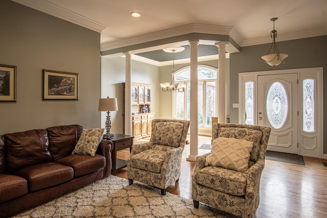 living room featuring ornamental molding, a chandelier, decorative columns, and wood finished floors