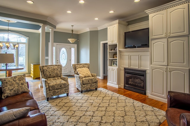 living room featuring a glass covered fireplace, wood finished floors, decorative columns, and an inviting chandelier