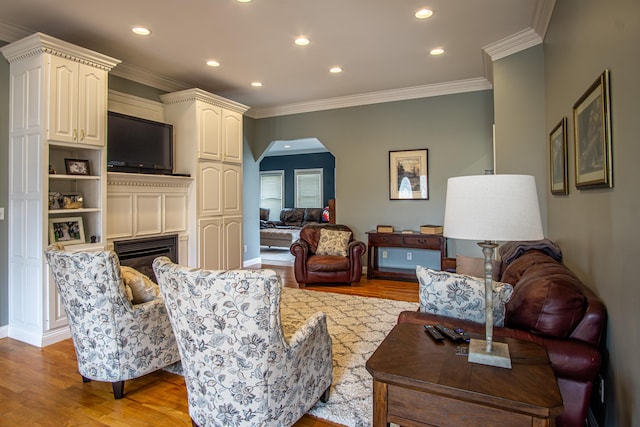 living room with arched walkways, light wood finished floors, ornamental molding, and recessed lighting