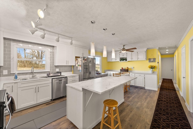 kitchen featuring a center island, appliances with stainless steel finishes, dark wood-type flooring, white cabinetry, and a sink