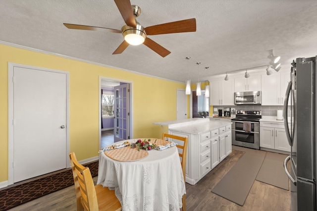 kitchen featuring stainless steel appliances, ornamental molding, white cabinetry, a kitchen island, and wood finished floors