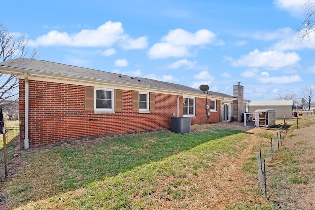 rear view of property featuring brick siding, fence, central AC, and a lawn