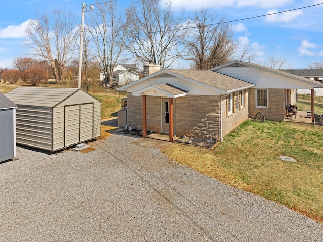 view of side of property featuring gravel driveway, a shingled roof, a shed, stone siding, and an outdoor structure