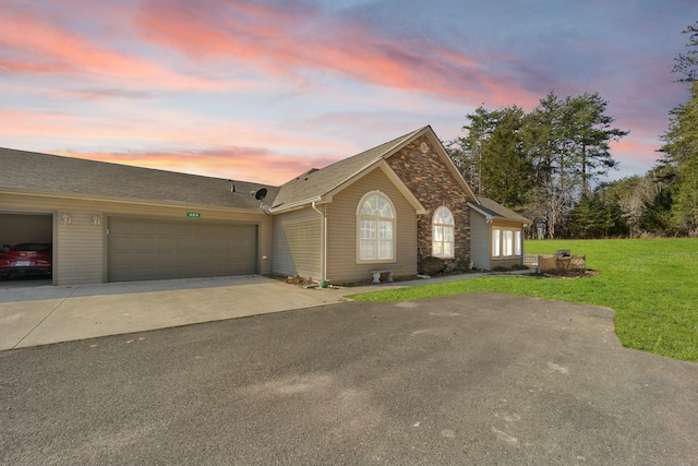 view of front of home featuring an attached garage, driveway, a yard, and stone siding