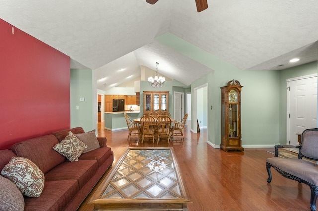 living room with vaulted ceiling, a textured ceiling, wood finished floors, baseboards, and ceiling fan with notable chandelier