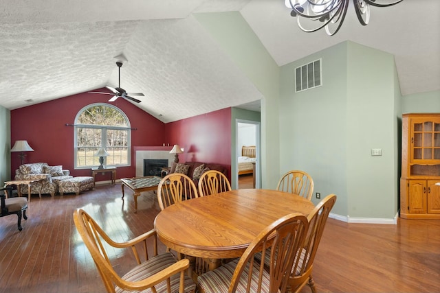 dining room with a tile fireplace, visible vents, vaulted ceiling, and hardwood / wood-style flooring